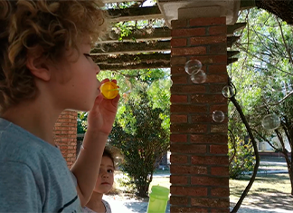 niño sopla en el parque haciendo burbujas para un experimento de aire