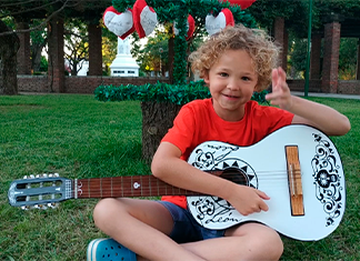 niño sentado tocando guitarra en la plaza