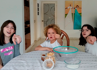tres niños en una mesa señalan la cámara