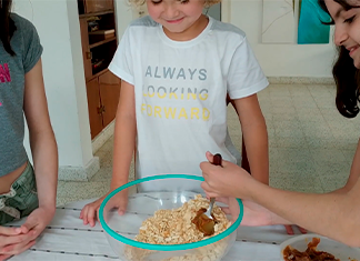 niña pone dulce de leche en un bowl de masitas molidas